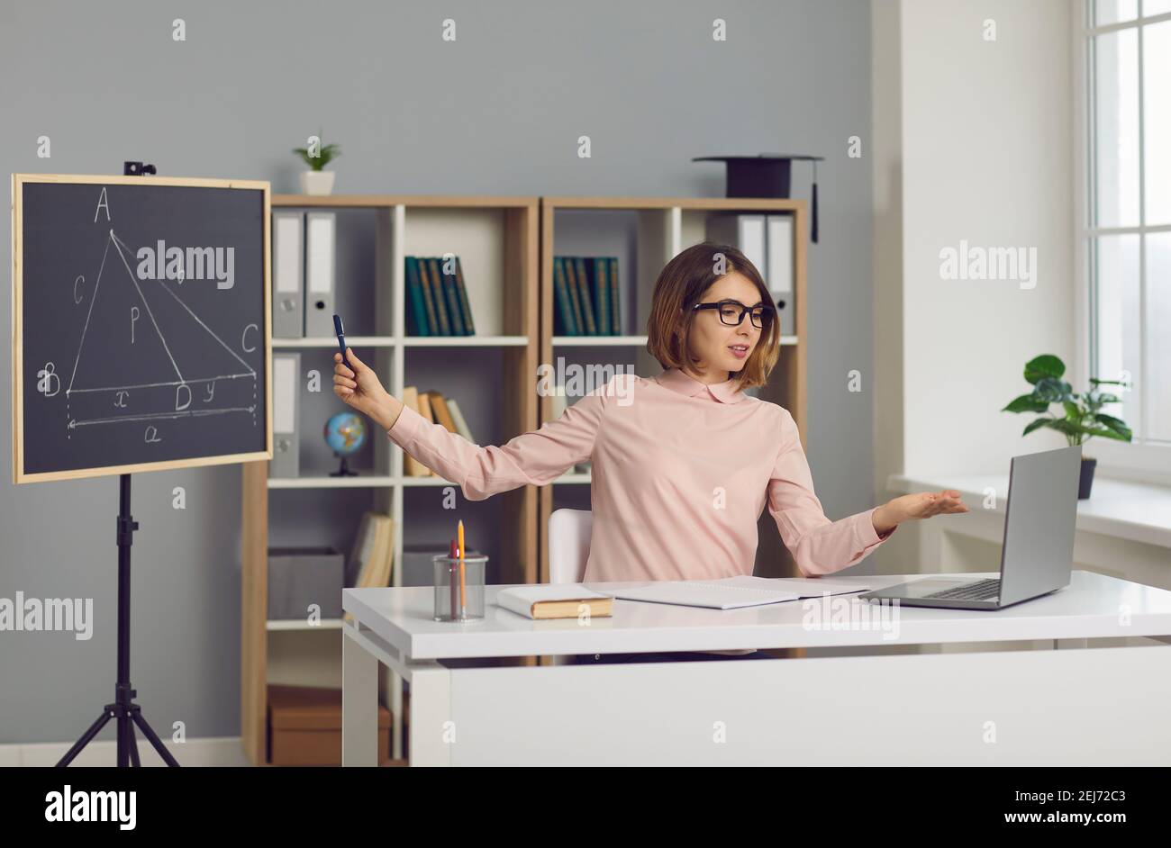 Insegnante di matematica della scuola seduto alla scrivania con il laptop e dare lezione di geometria online Foto Stock