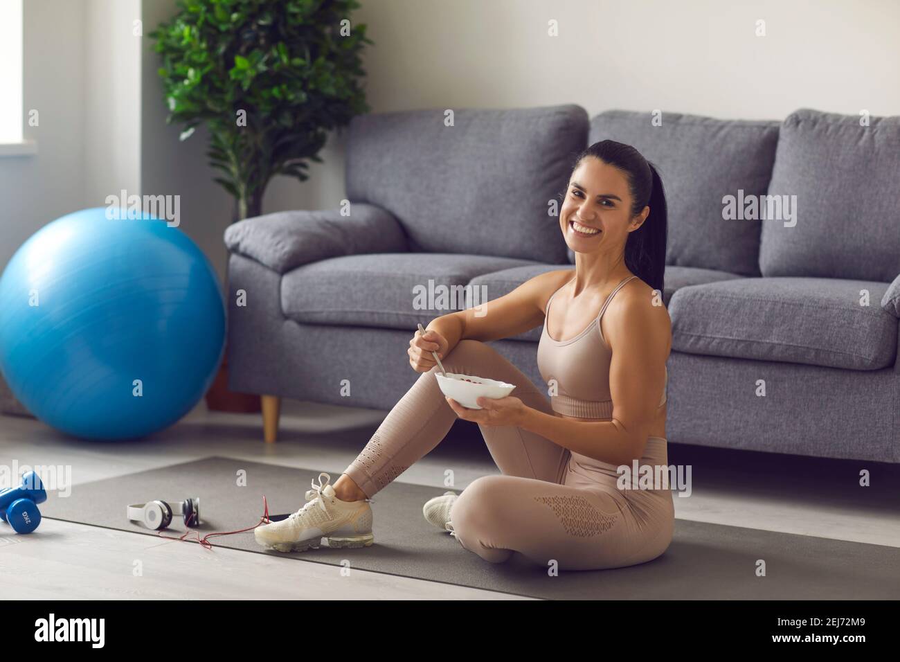 Allegra fitness lady in abbigliamento sportivo seduto sul tappetino fitness e. mangiare sano pasto nutriente equilibrato Foto Stock