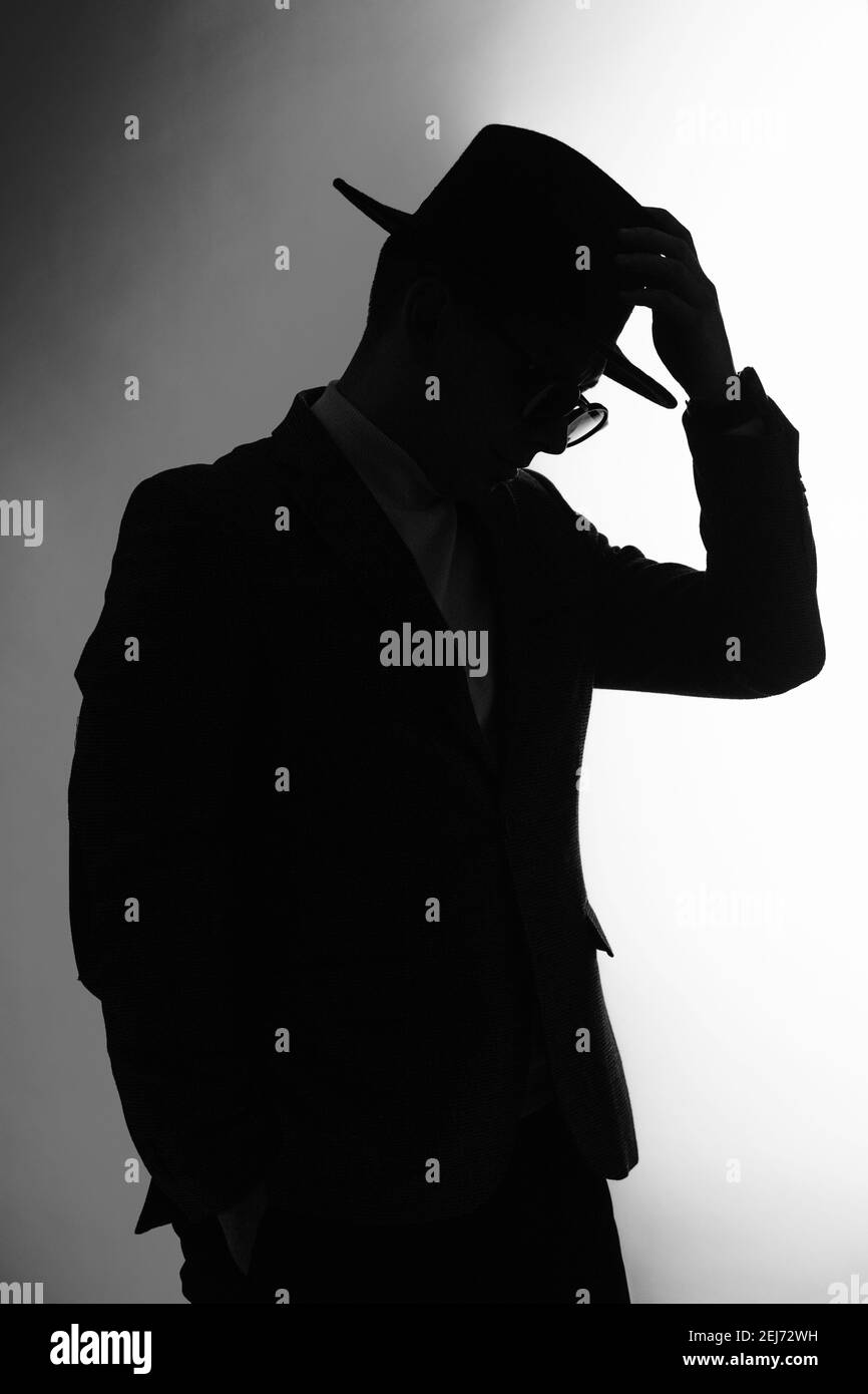 Silhouette scura di un uomo in una giacca, occhiali da sole e mano su un cappello classal Foto Stock