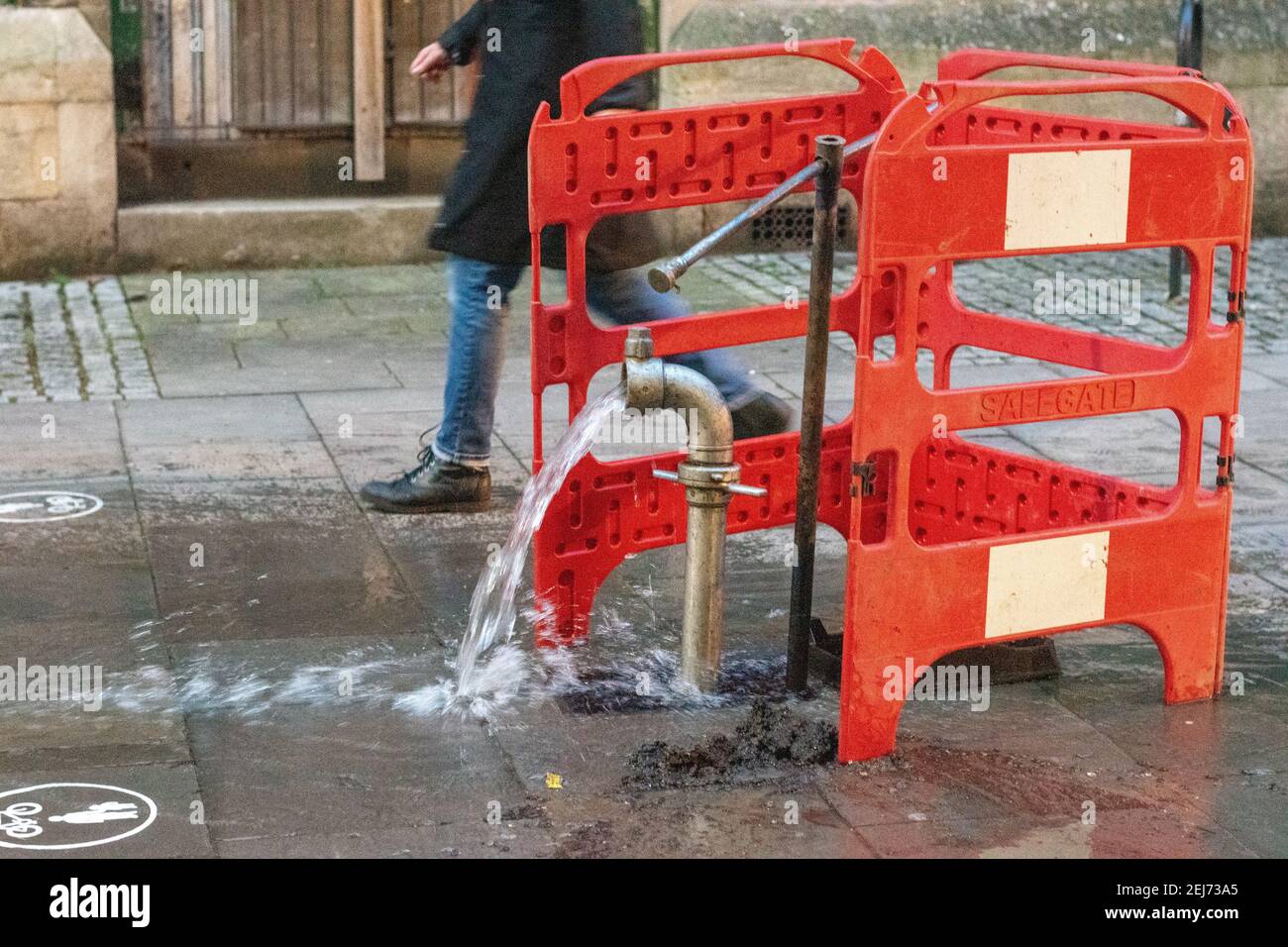 Burst acqua pipe in una strada urbana con pedonale a piedi in background Foto Stock