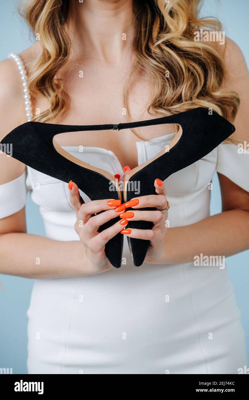 Donna in un abito bianco che tiene scarpe con tacco alto in balck insieme tagliato, senza viso. Foto Stock