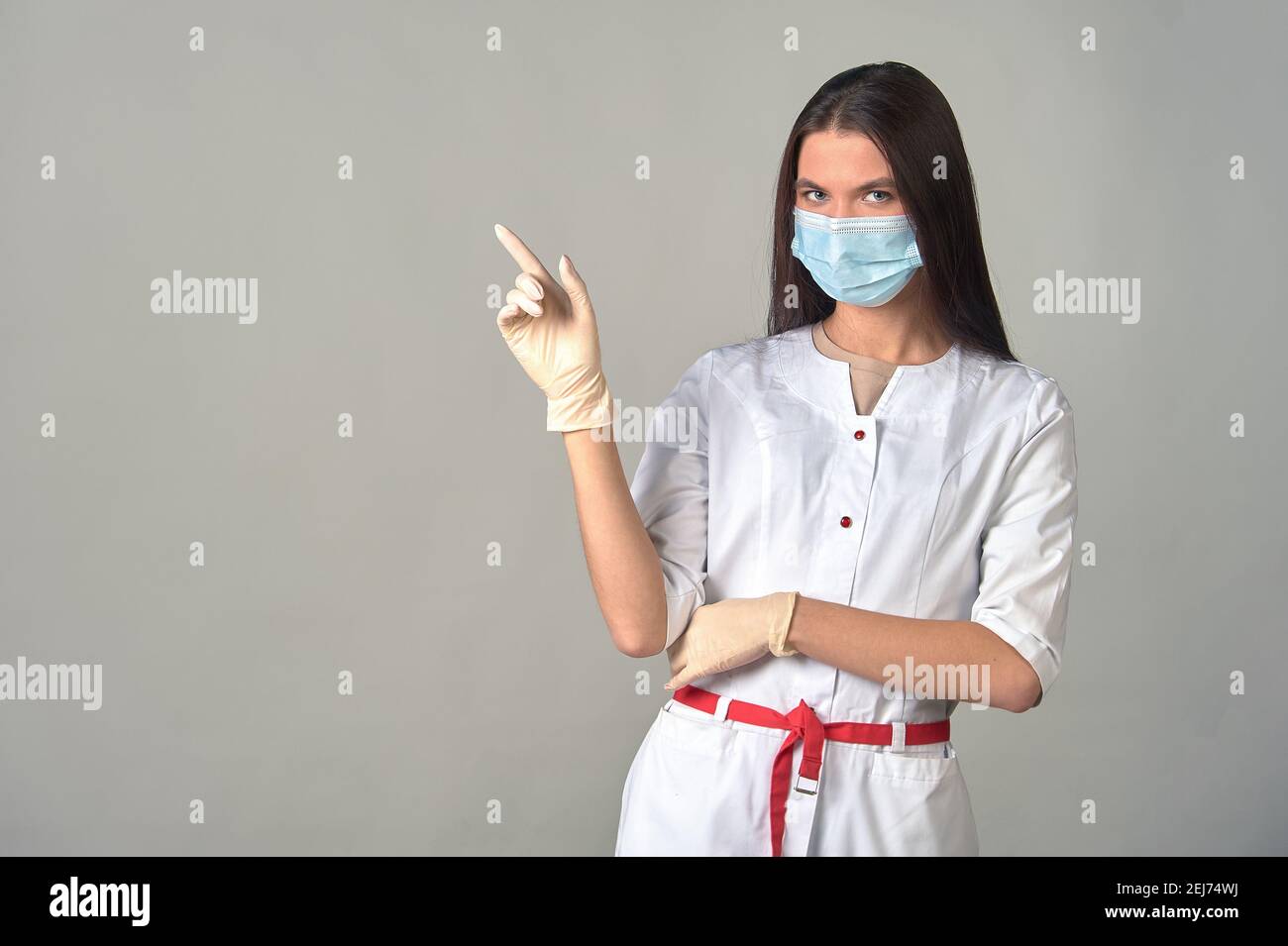 una dottoressa attenta in un abito medico, maschera e guanti, che avverte su qualcosa di importante. Foto Stock