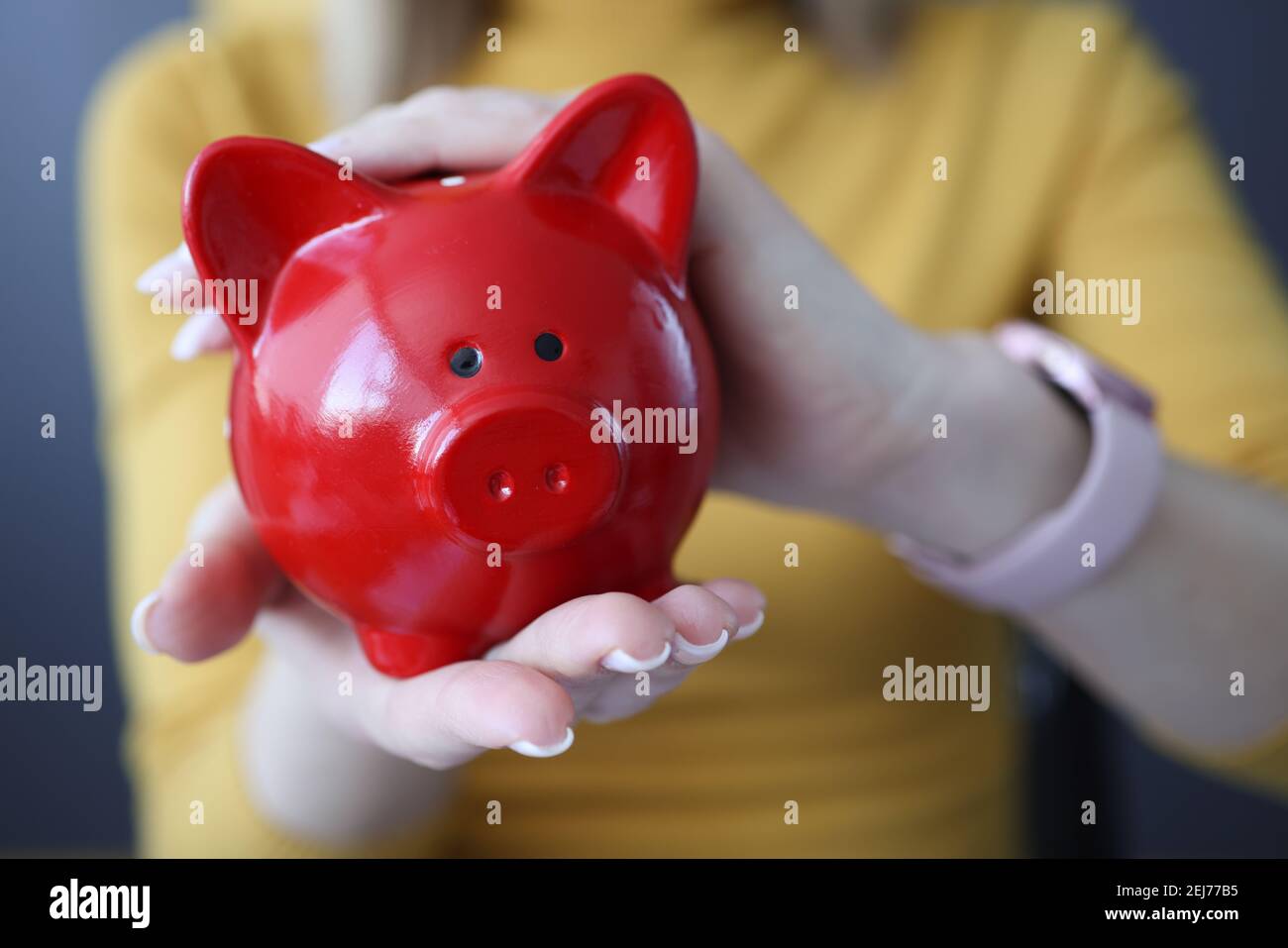 Donna che tiene la banca del piggy rosso nel suo closeup delle mani Foto Stock