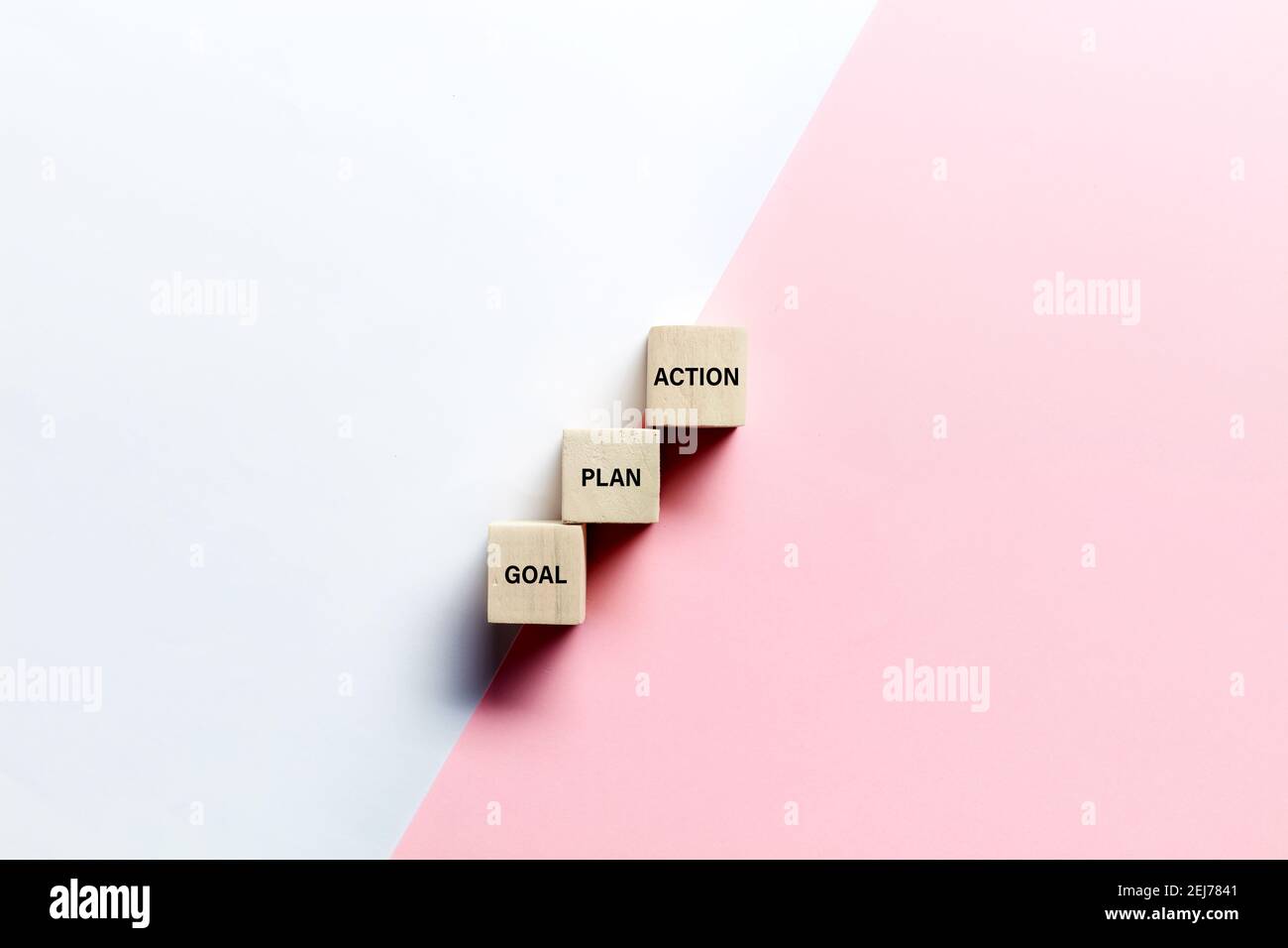 Le parole obiettivo, piano e azione su cubi di legno su sfondo rosa e bianco. Concetto di strategia di pianificazione aziendale o di marketing. Foto Stock