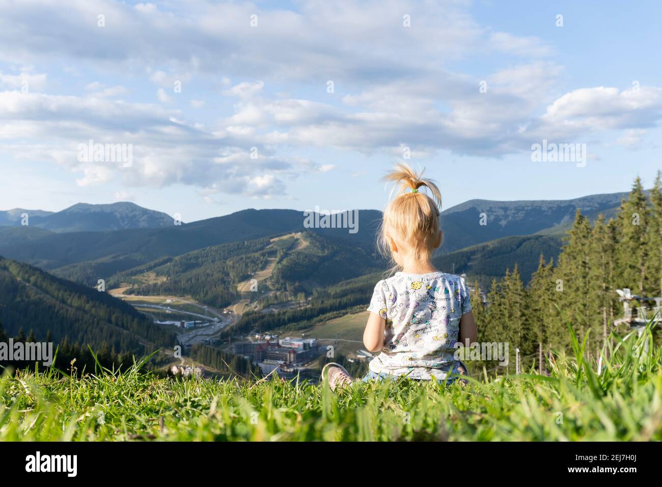 Bambino seduto su erba verde nella parte superiore del collina con vista sulle montagne Foto Stock