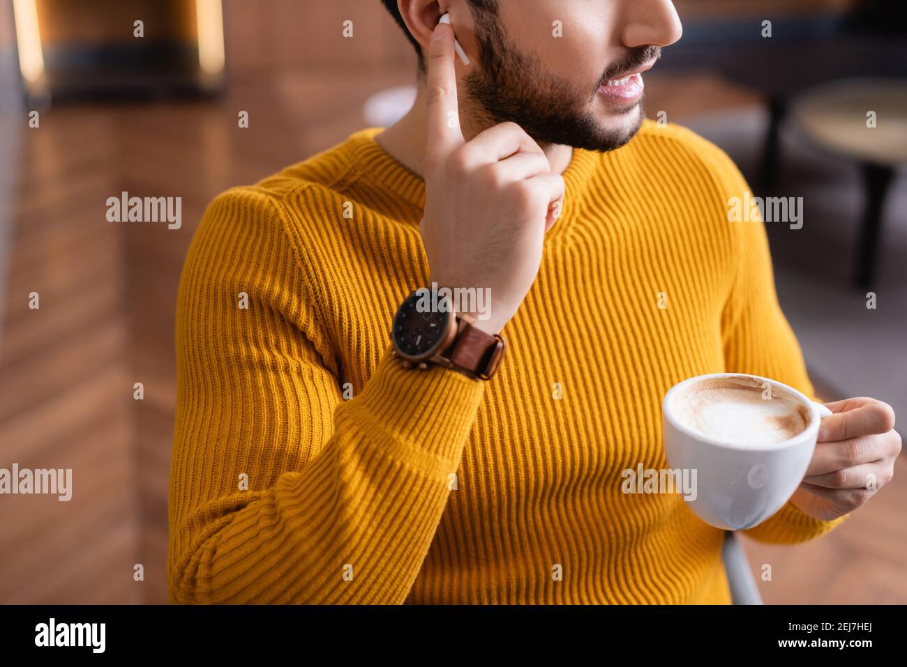 vista ritagliata dell'uomo arabo che regola l'auricolare mentre tiene la  tazza di caffè nel ristorante Foto stock - Alamy