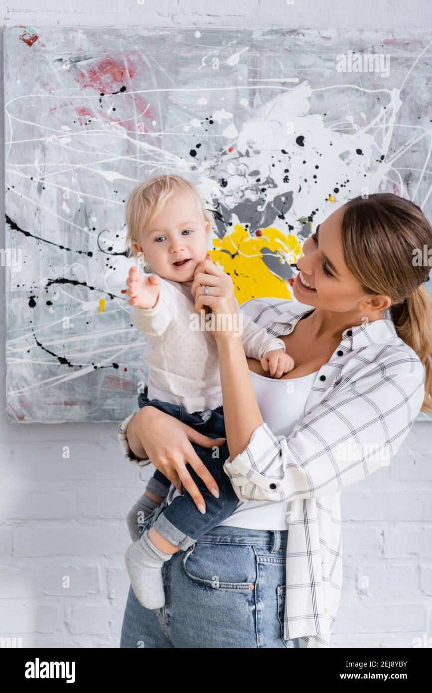 sorridente madre che tocca la guancia del piccolo figlio mentre lo tiene a casa Foto Stock