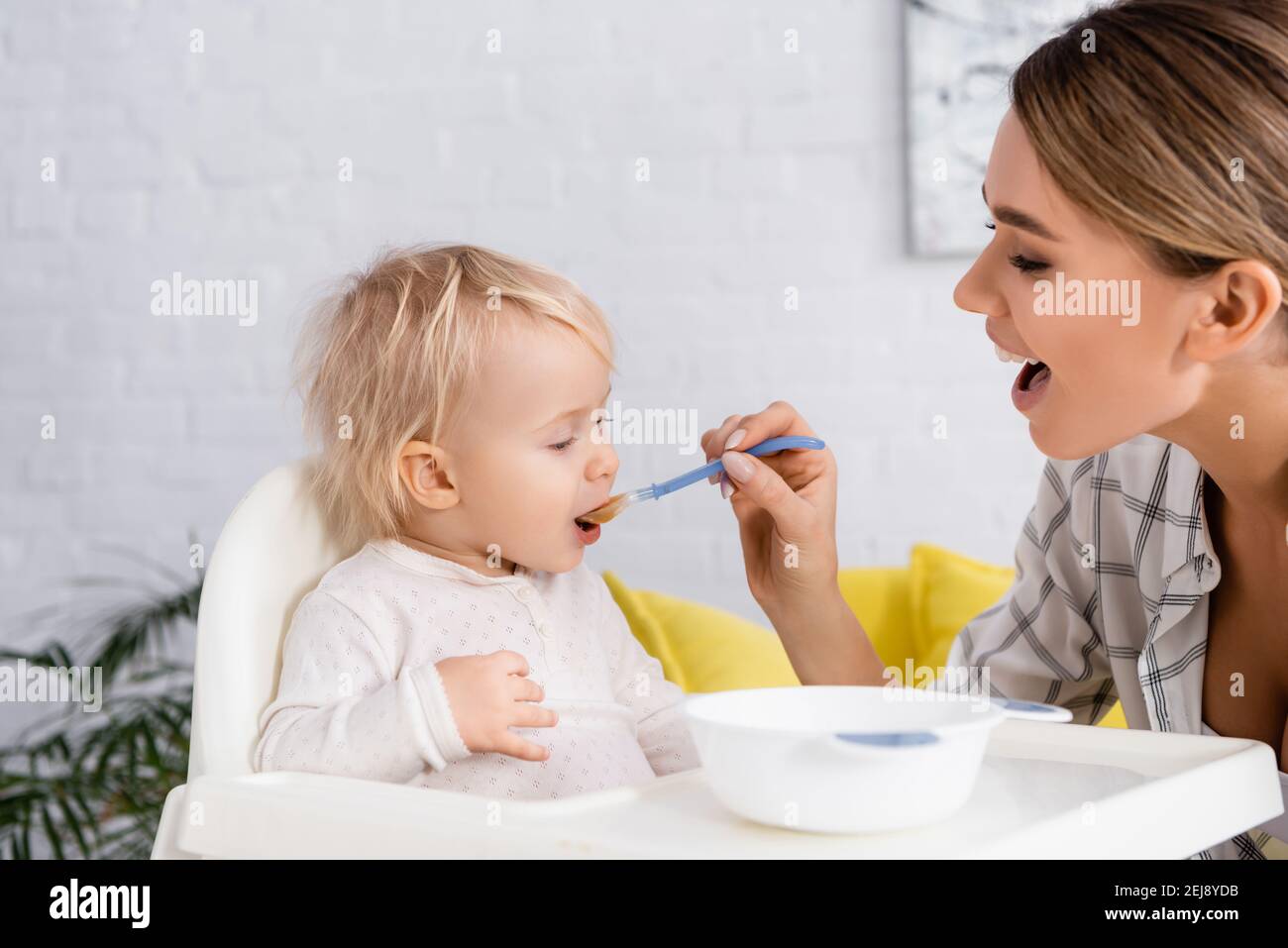 giovane donna con bocca aperta che alimenta il figlio del bambino a casa Foto Stock