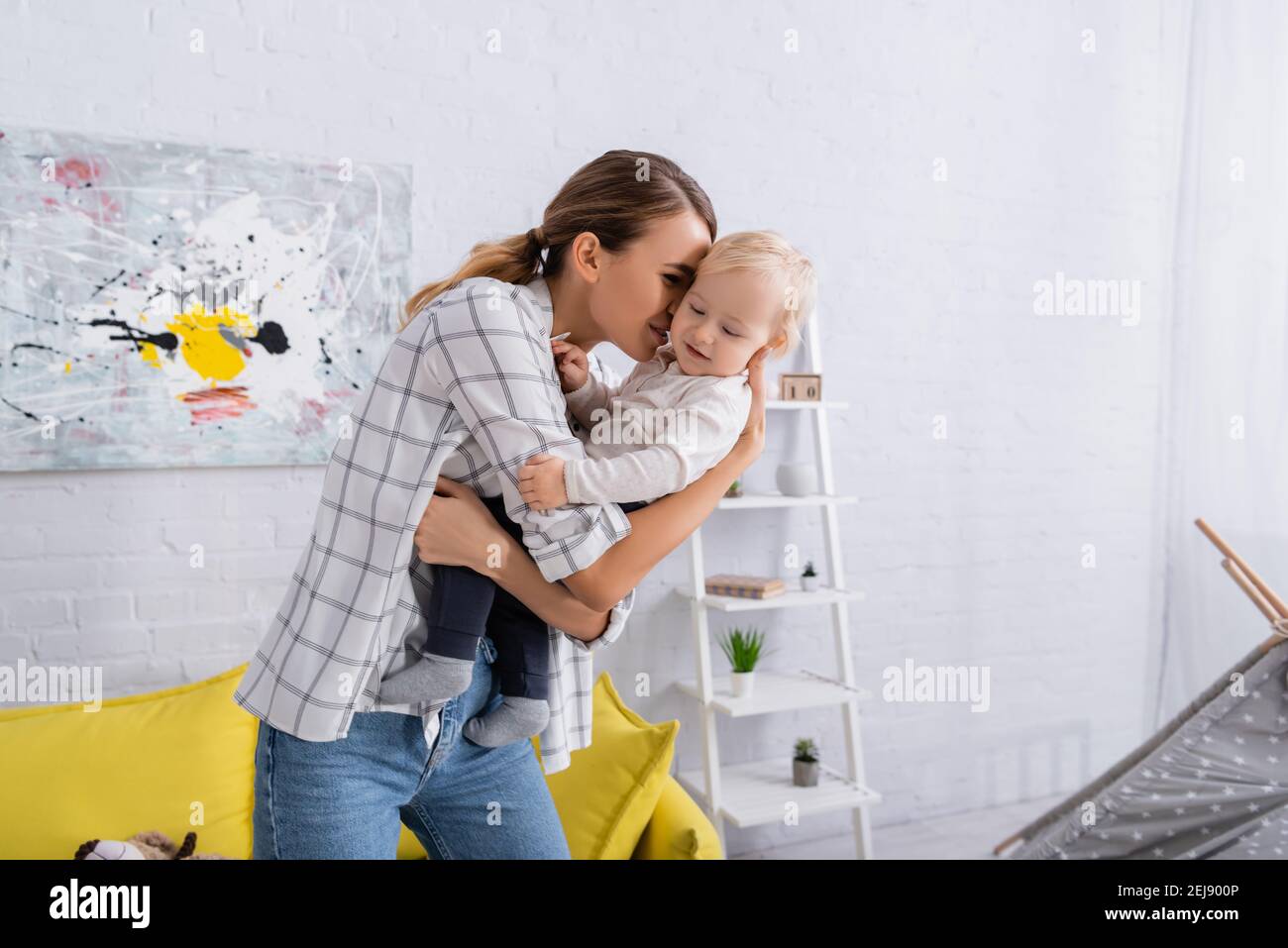 giovane donna che tiene e abbraccia il figlio del toddler a casa Foto Stock