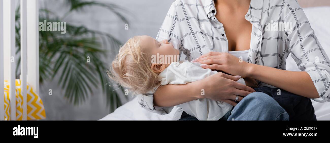 donna lulling bambino ragazzo mentre si siede a casa, banner Foto Stock