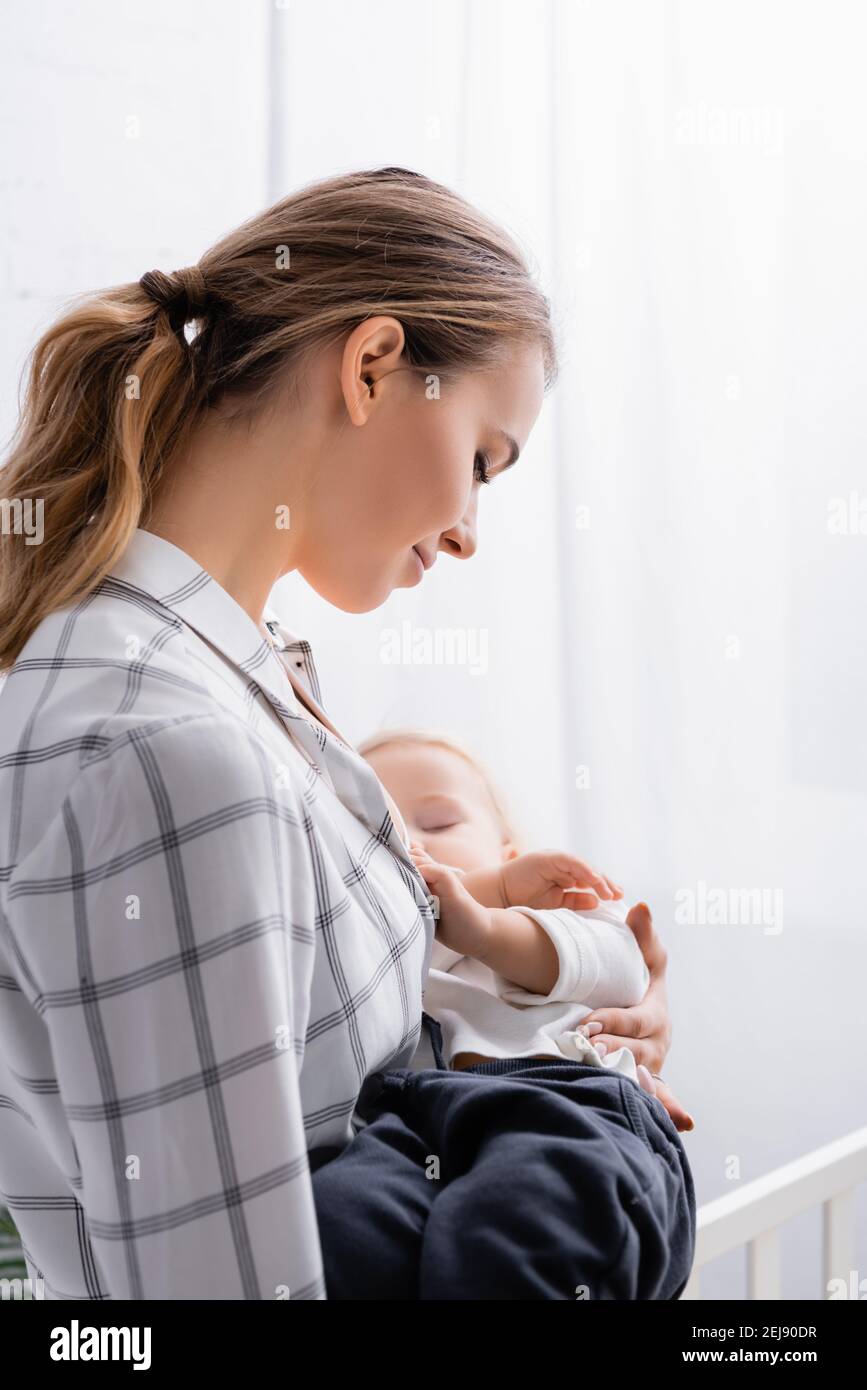 giovane donna sorridente lulling bambino a casa Foto Stock