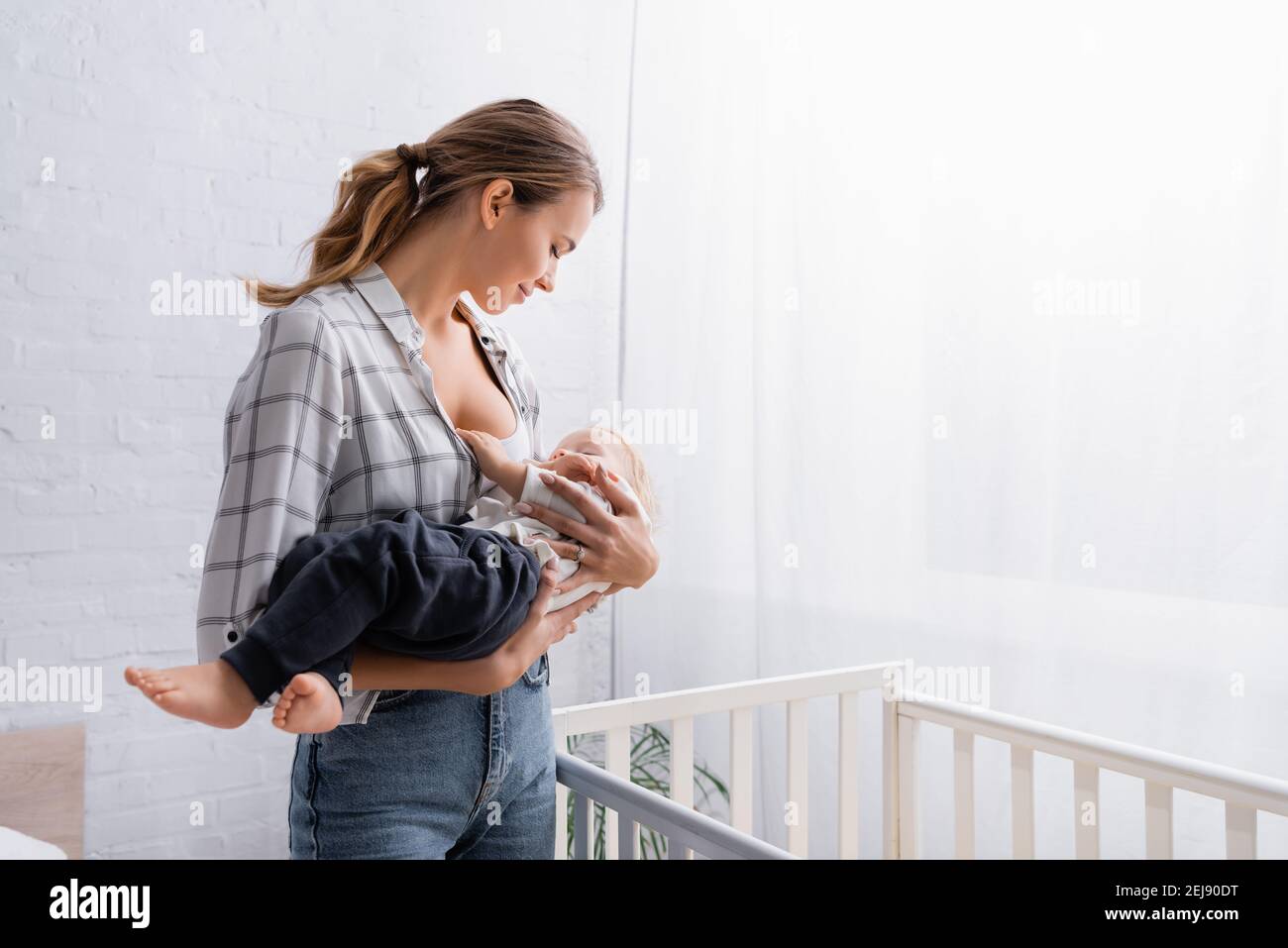 felice giovane donna lulling piccolo figlio vicino al presepe a casa Foto Stock