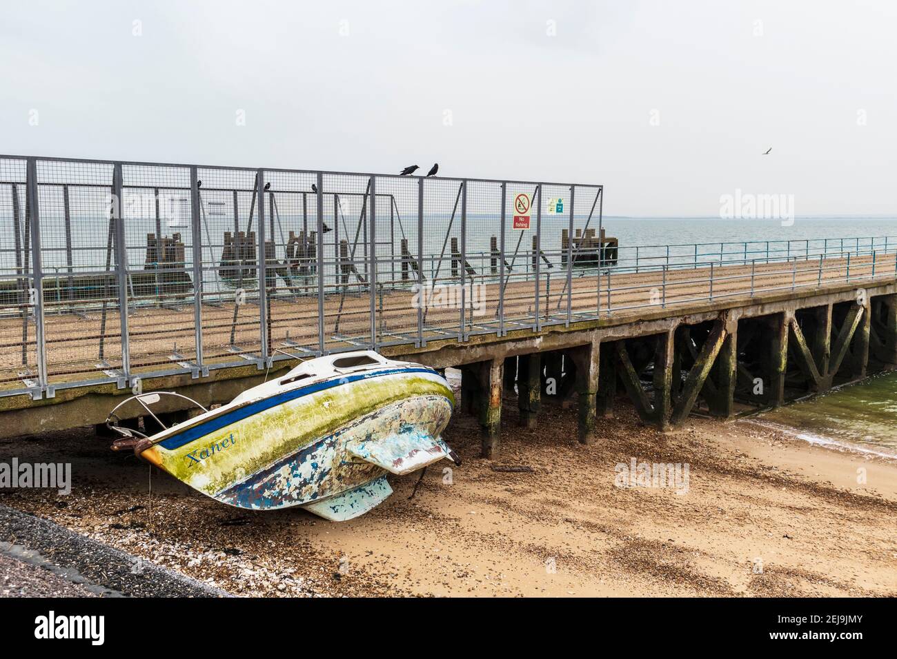 Derelict Yacht 'Xanet' abbandonato sulla spiaggia a Shoeburyness contro Old Molo di chiatta Foto Stock