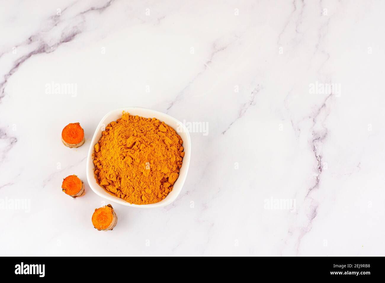 Ciotola con polvere curcuma con diverse radici della stessa pianta su un tavolo di marmo. Concetto di medicina naturale e omeopatia Foto Stock
