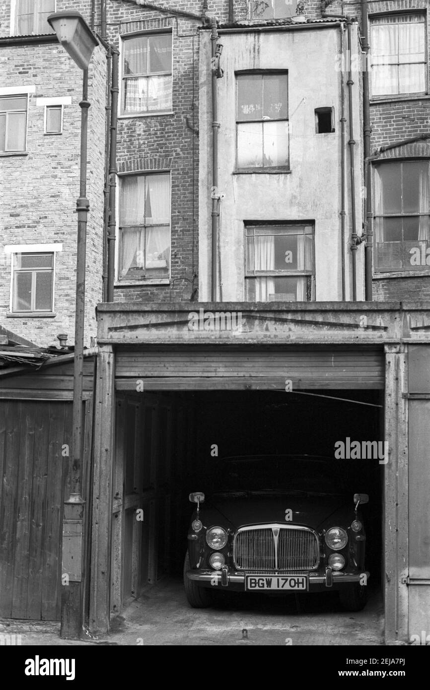 UK, West London, Notting Hill, 1973. Rundown e faticosamente grandi case a quattro piani stanno iniziando ad essere restaurate e ridecorate. Powis Mews garage con una Rover P5 salone auto parcheggiata all'interno. Vista sul retro dell'alloggiamento su Powis Terrace. Foto Stock