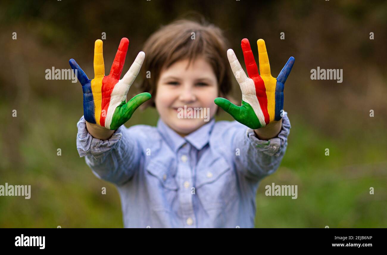 Ritratto esterno di allegra ragazza capretto mostra ciao gesto con mani dipinte in colori bandiera Seychelles. Concentrarsi sulle mani Foto Stock