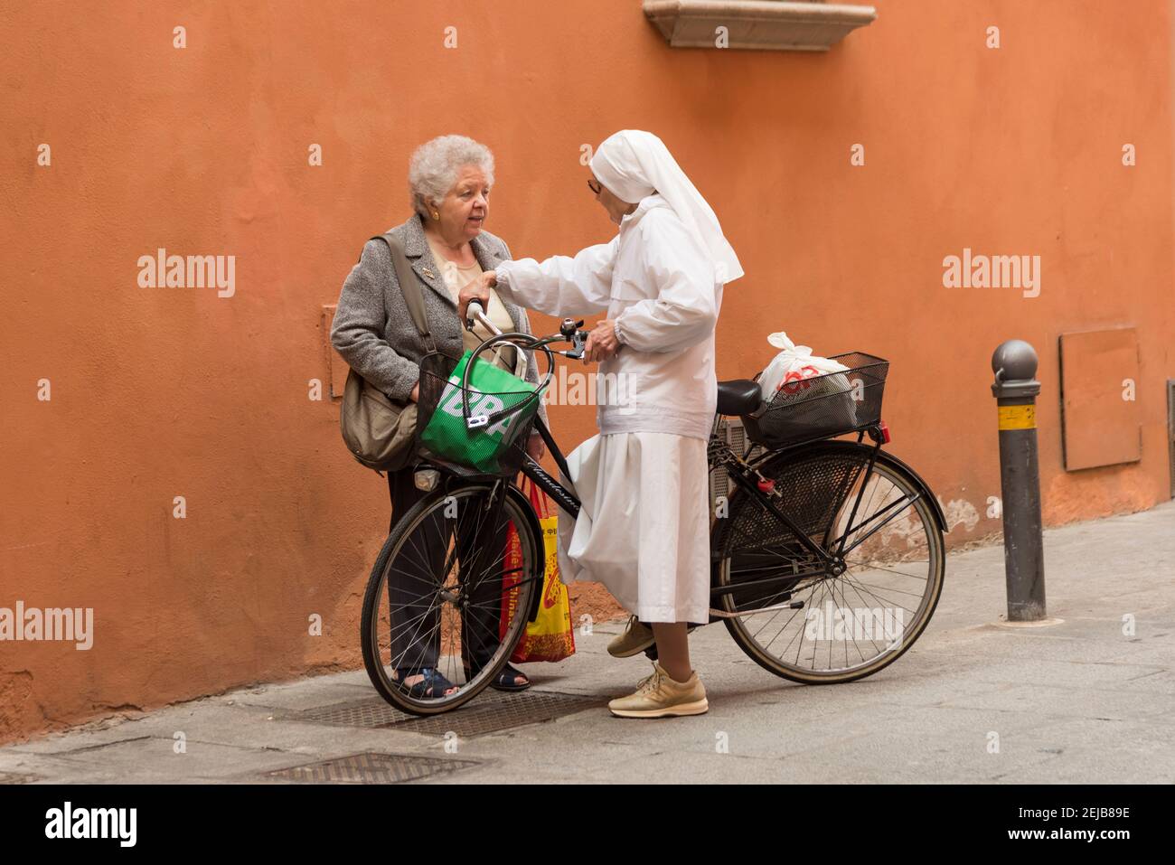 Una suora in un'abitudine bianca con una chiacchierata in bicicletta Con una donna in una strada a Bologna Italia Foto Stock