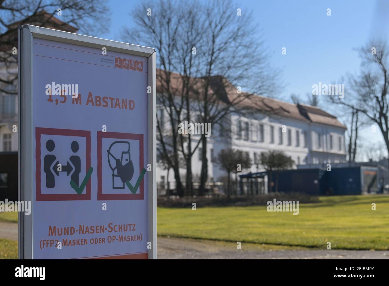 Oranienburg, Germania. 22 Feb 2021. Un cartello che chiede alla gente di mantenere la distanza e di indossare una maschera si erge su un sentiero a Schloßpark sullo sfondo del castello. Il distretto di Oberhavel aveva approvato la riapertura del parco in condizioni rigorose. Ad esempio, i visitatori devono osservare le regole della distanza e, ad eccezione dei bambini di età inferiore ai sei anni, indossare una maschera FFP2 o medica. Credit: Soeren Stache/dpa-Zentralbild/dpa/Alamy Live News Foto Stock