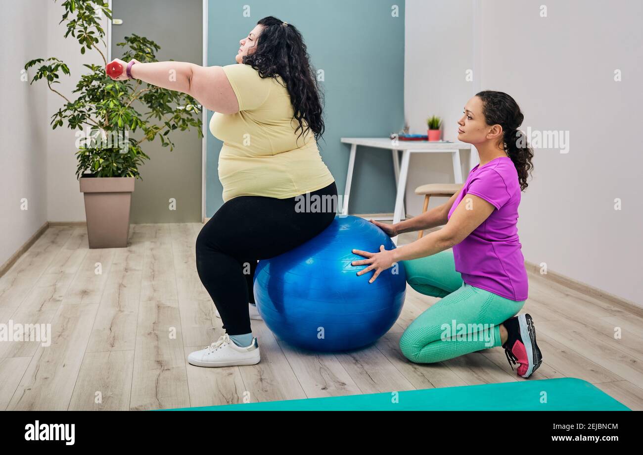 Donna in sovrappeso che fa esercizi con il suo allenatore per la perdita di peso uso di manubri e palla fitness Foto Stock