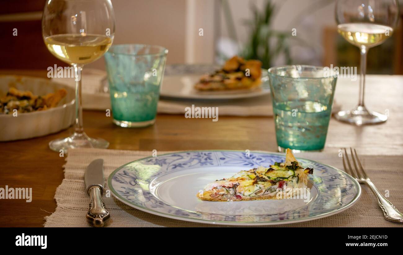 Pranzo festivo con gli amici, quiche vegetariane fatte in casa con zucchine, bietole e formaggi svizzeri, vino bianco. Bicchieri d'acqua turchese. Foto Stock