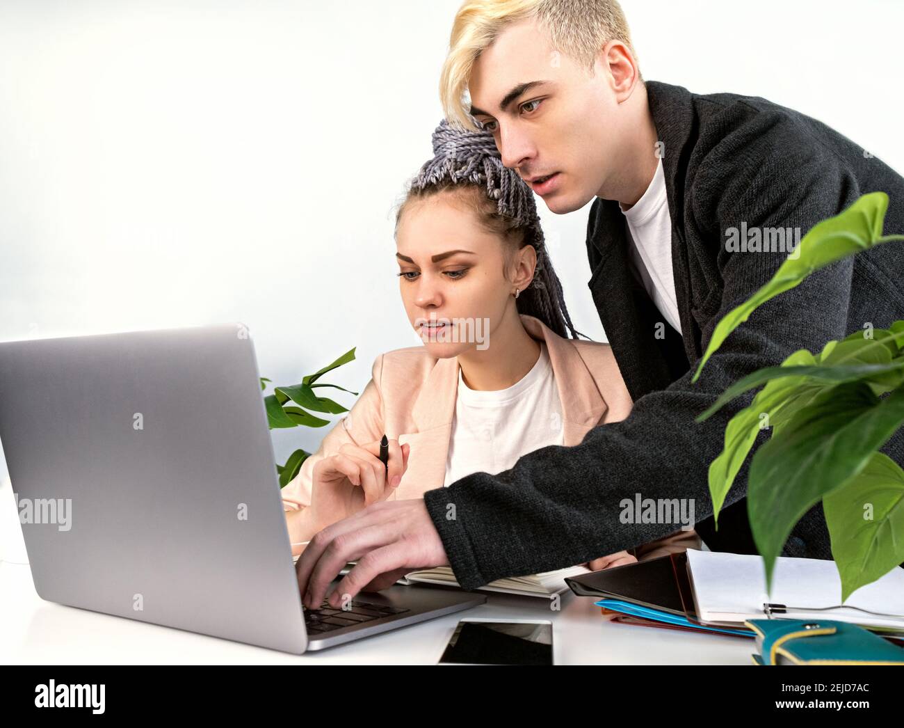 Lavorare in ufficio, in ufficio. Giovane uomo attraente che aiuta la sua collega femminile ad affrontare il progetto. Si è appoggiato sopra il suo laptop, in piedi accanto a. Foto Stock