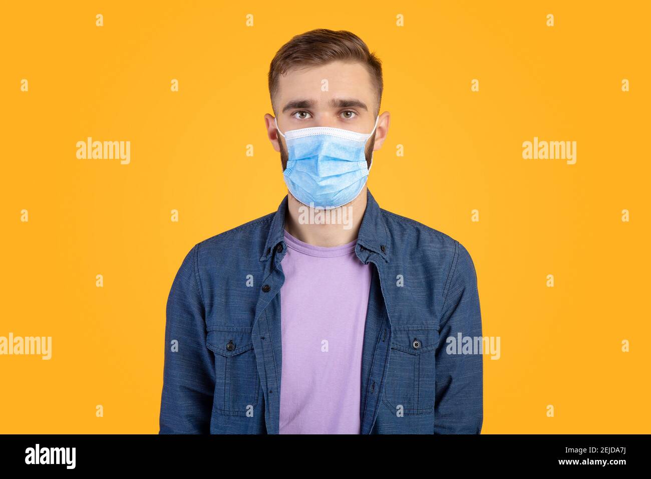 Ritratto di uomo caucasico in maschera medica guardando la fotocamera su sfondo arancione studio. Concetto di allontanamento sociale Foto Stock