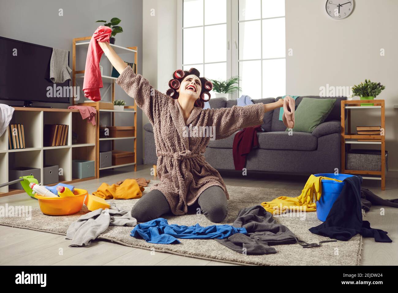 La casalinga stanca piangendo mentre pulisce il mess e raccogliendo in su vestiti sparsi dal pavimento Foto Stock
