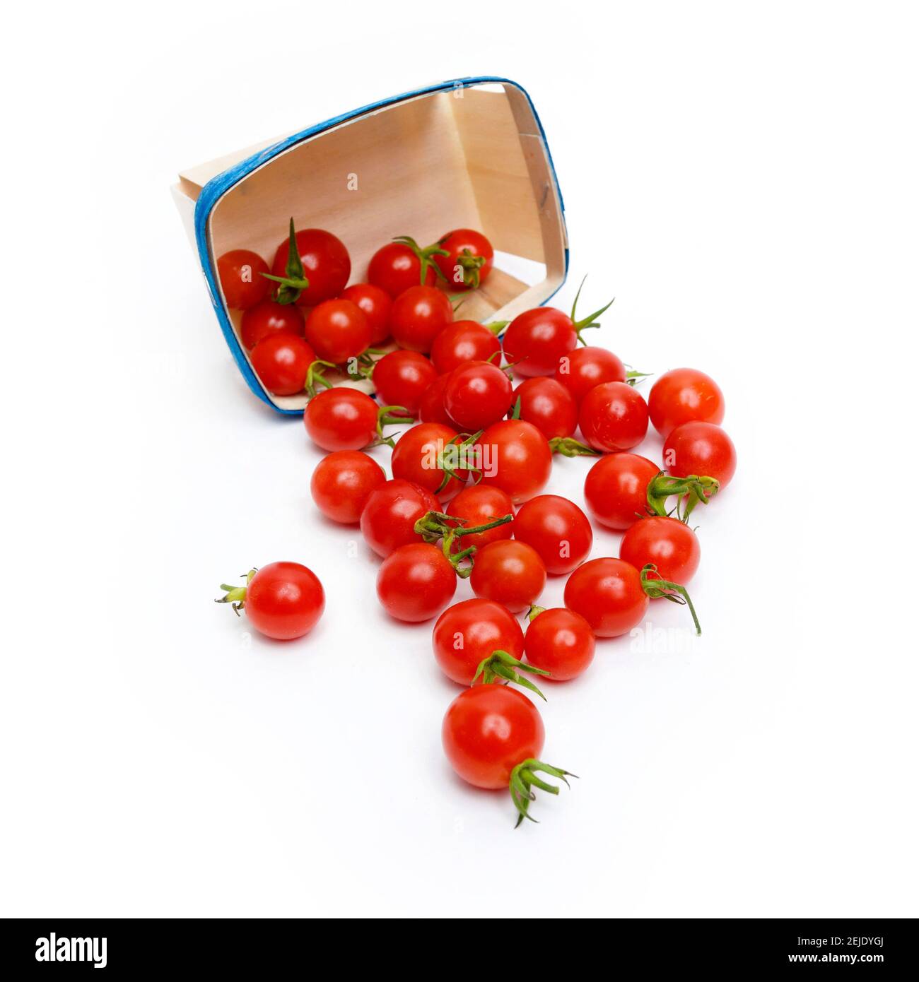 I pomodori ciliegini freschi fuoriescono da un contenitore blu su sfondo bianco durante una sessione di preparazione della cucina Foto Stock