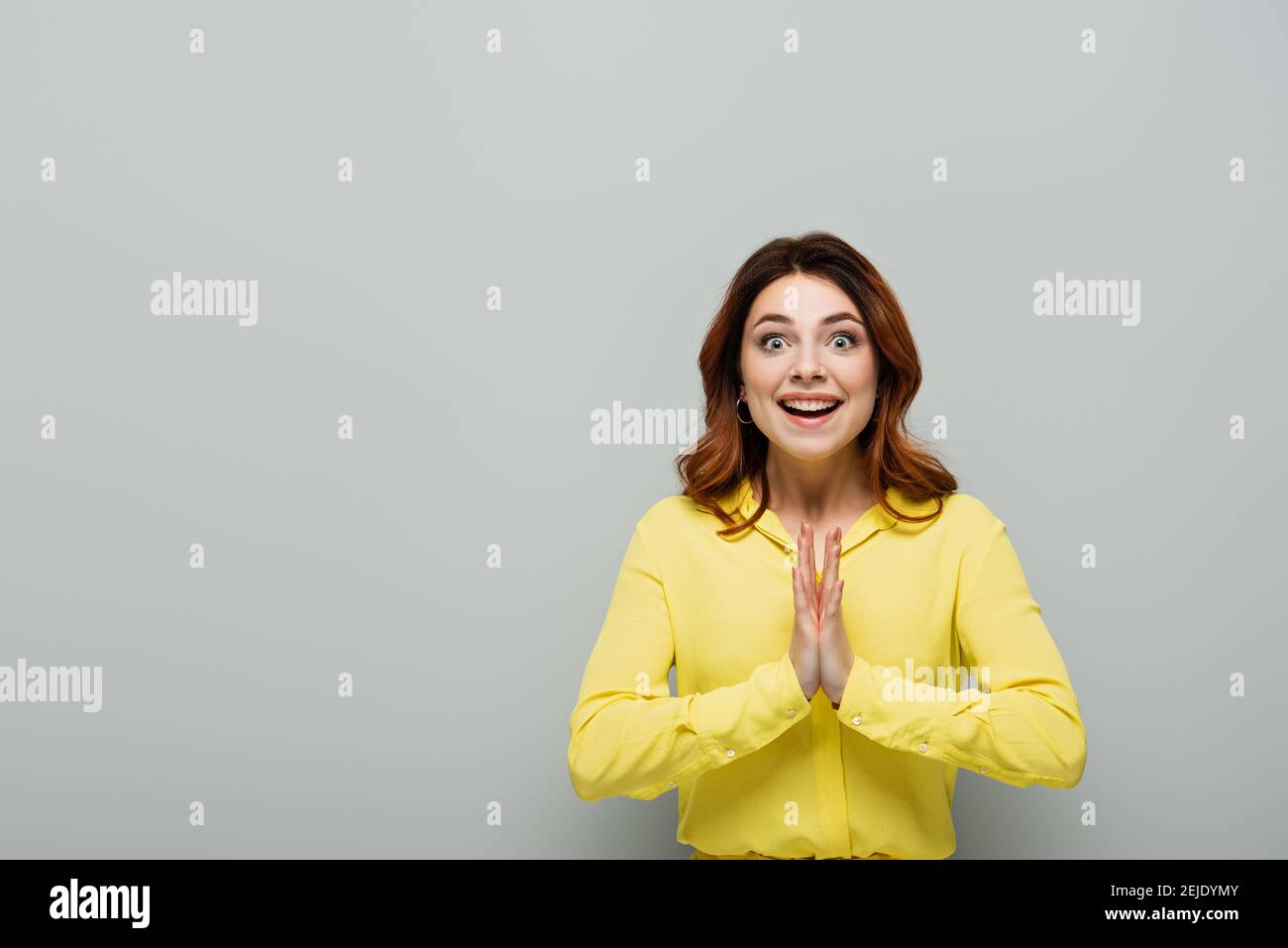 donna allegra che batte le mani e sorride alla macchina fotografica su grigio Foto Stock