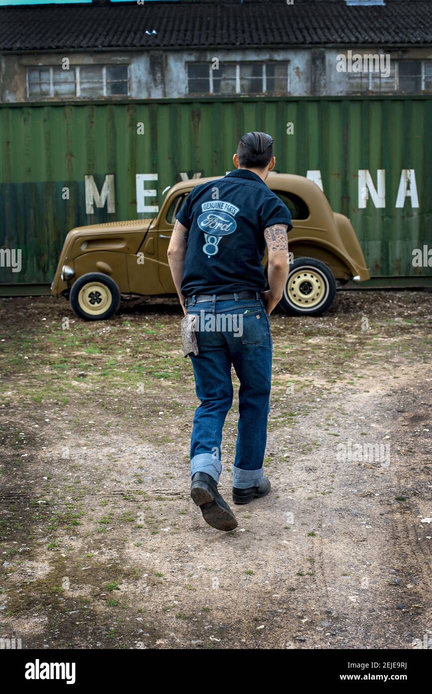 Ford popolare 1958 Hot Rod vista posteriore di giovane uomo in jeans che camminano a car.Rearview colpo di un uomo che cammina verso la sua auto parcheggiata. Foto Stock