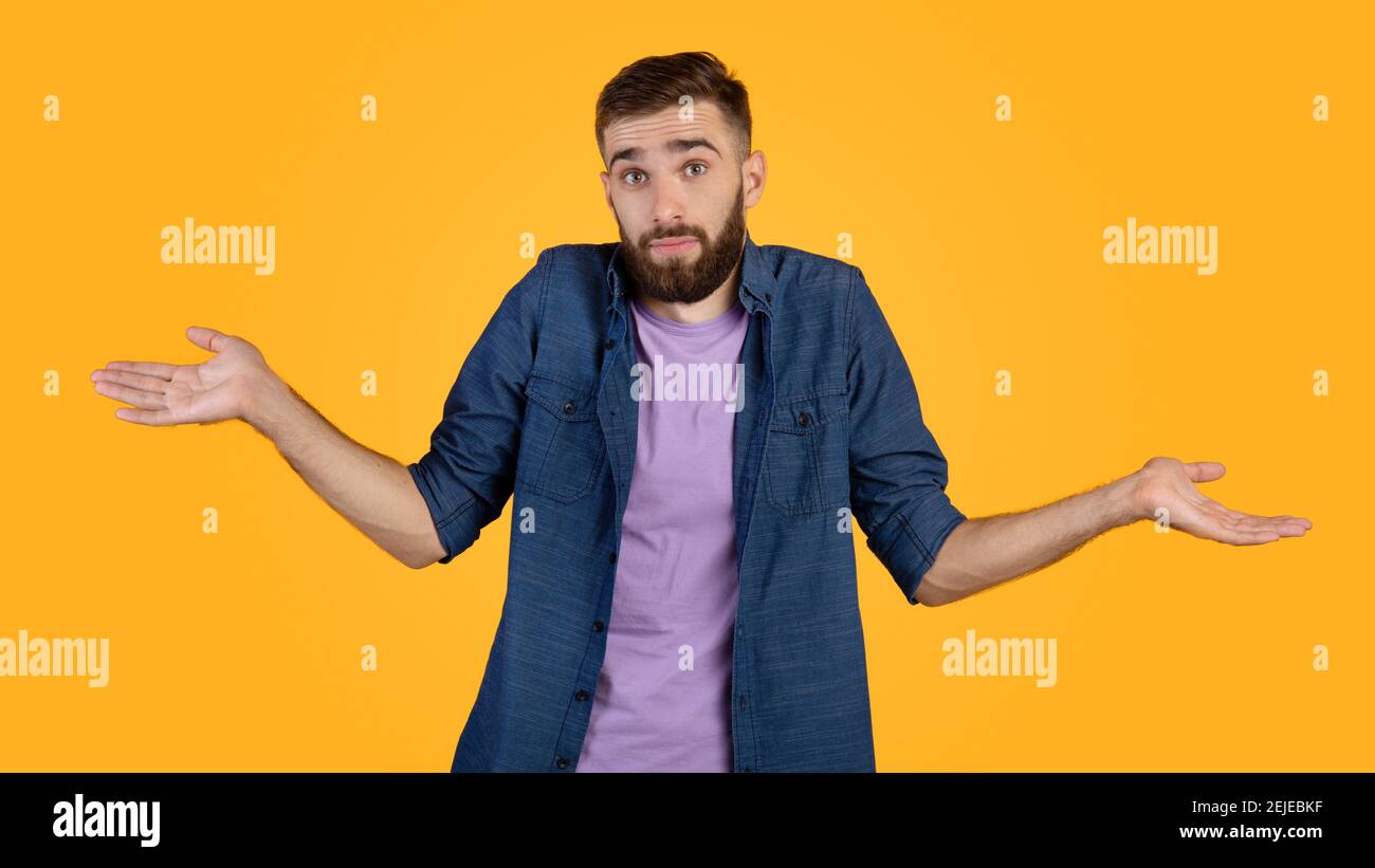Non lo so. Bel ragazzo caucasico che si infrange le spalle, sentendosi perplesso o incerto su sfondo arancione studio Foto Stock