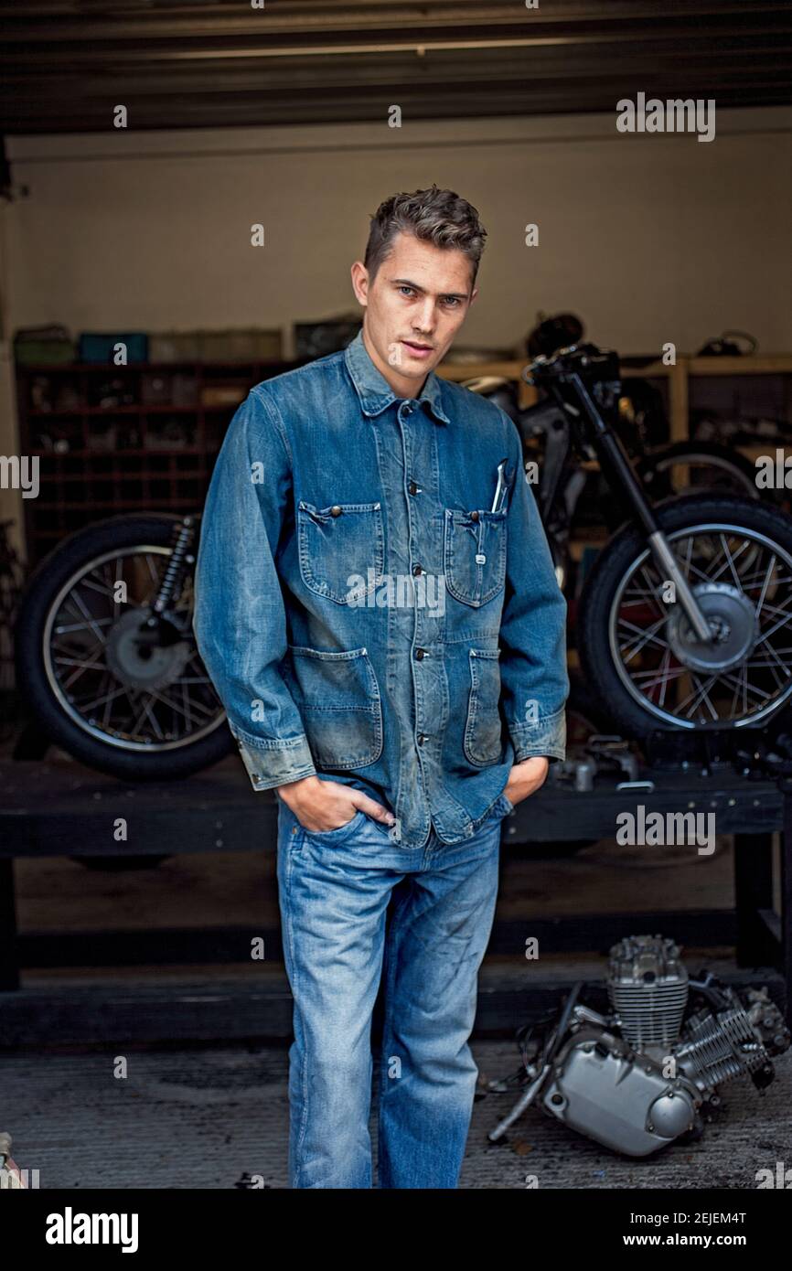 Giovane uomo che indossa un doppio denim in un laboratorio di motociclette. Foto Stock