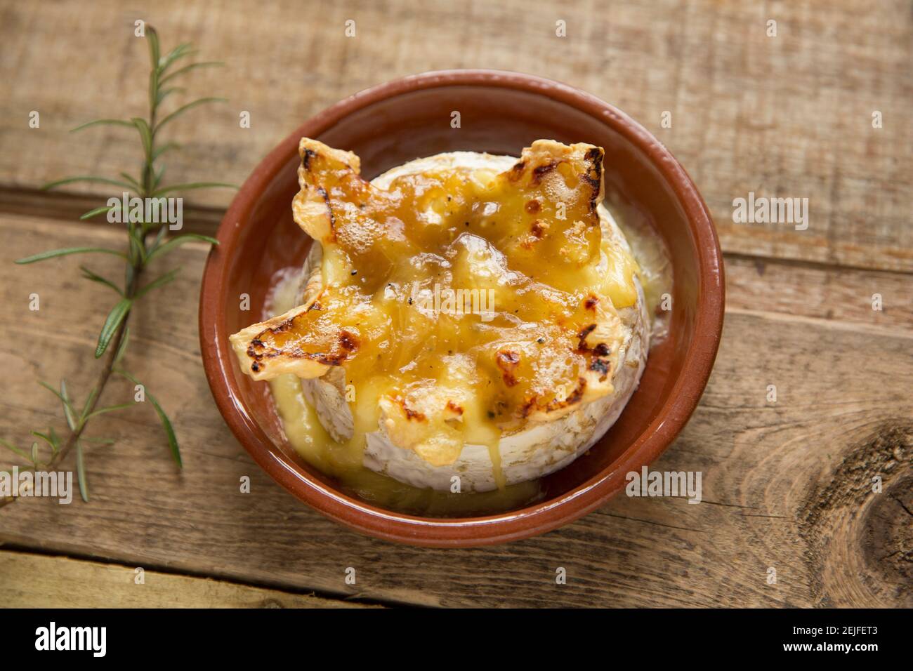 Camembert francese che è stato cotto in un forno con un tartufo, aglio e salsa al miele. Sfondo in legno guarnito con rosmarino. Inghilterra GB Foto Stock