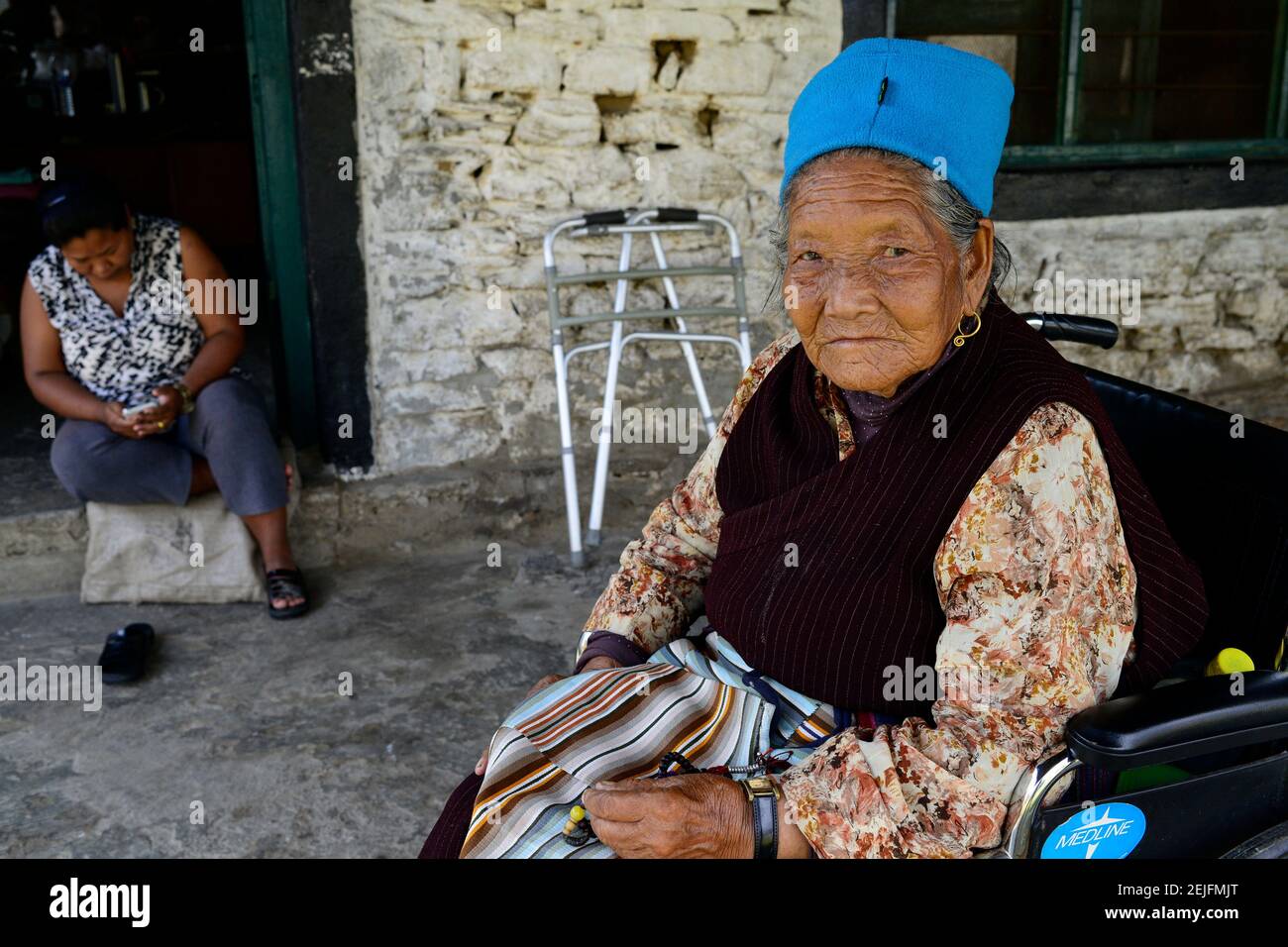 NEPAL Pokhara, campo profughi tibetano, vecchia donna con collana in preghiera in sedia a rotelle / tibetisches Fluechtlingslager Prithivi, alte Tibeterin bei einem Gebet mit Gebetskette im Rollstuhl Foto Stock