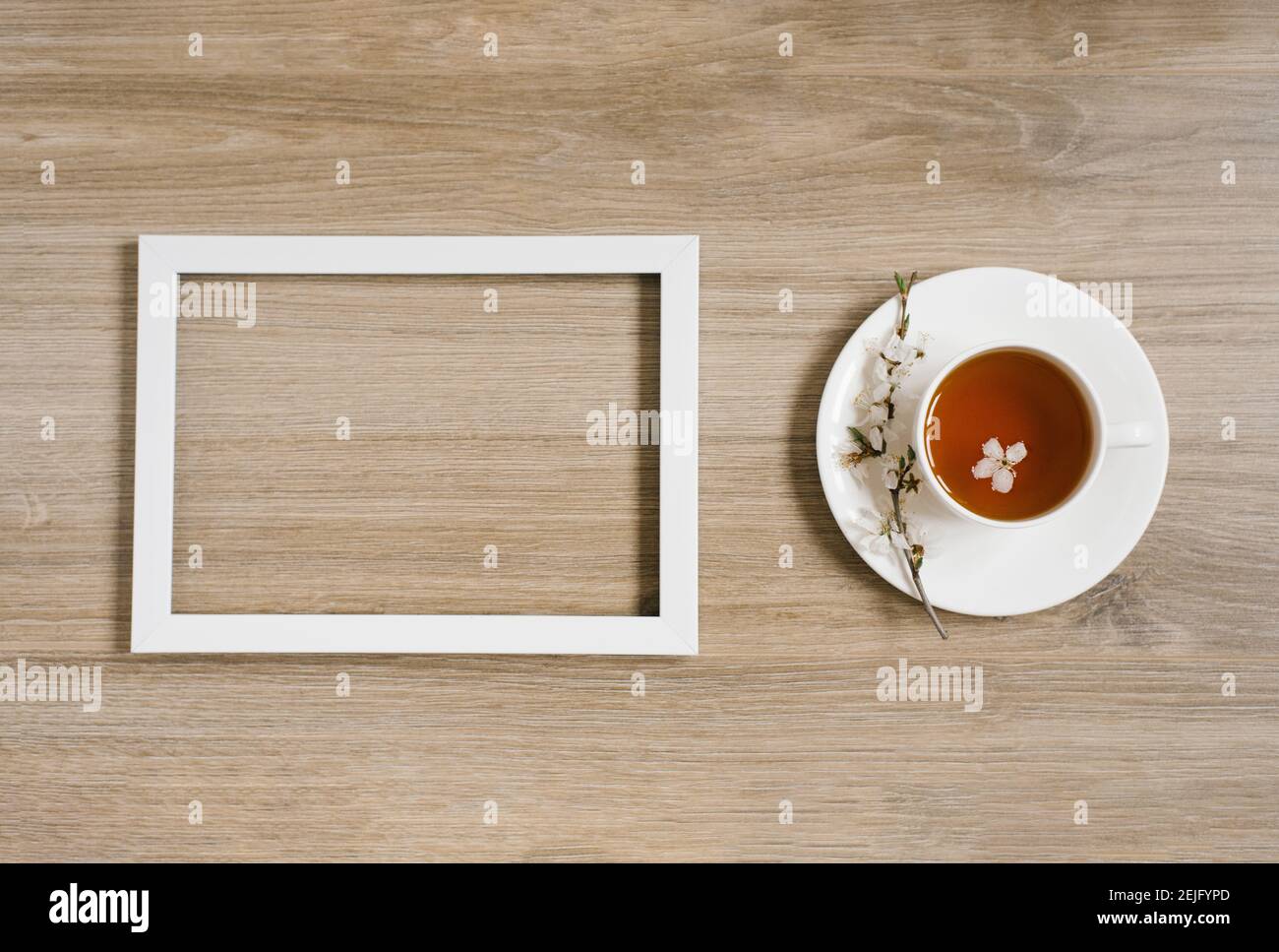 Una tazza bianca con tè nero e un trampino di fiori di mela e una cornice bianca su uno sfondo di legno. Mocap e su prostranstva Foto Stock