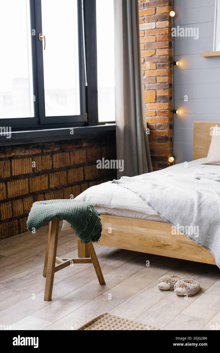 Una coperta verde è stesa su uno sgabello vicino al letto, in piedi. Vicino alla finestra. Casa scandinava Foto Stock