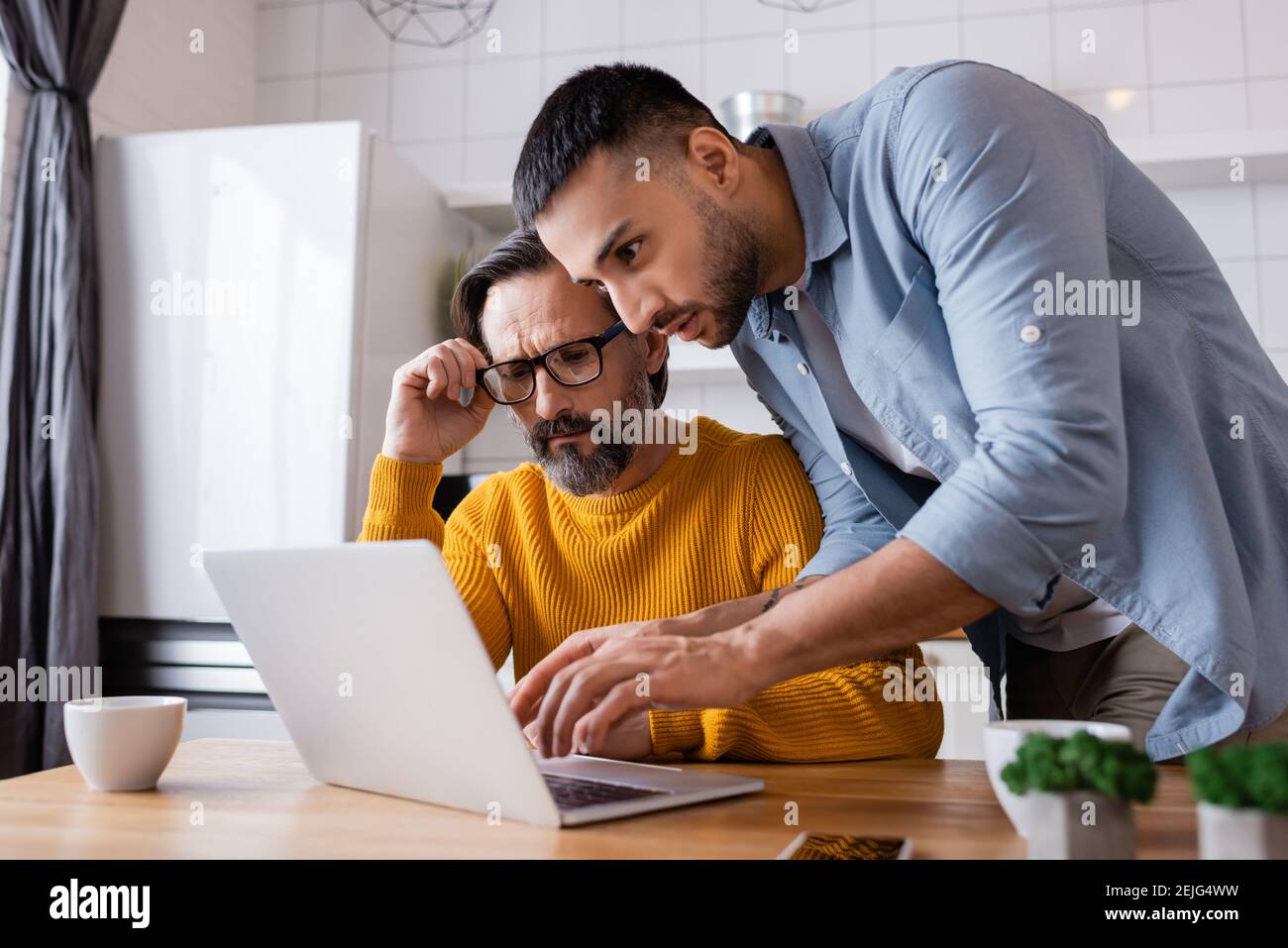 giovane uomo ispanico che scrive sul laptop vicino pensieroso padre che regola gli occhiali, primo piano offuscato Foto Stock