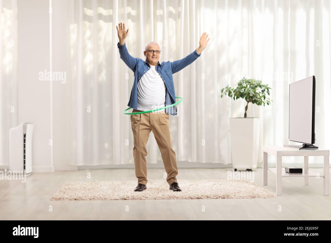 Uomo maturo che gira un cerchio di hula a casa in un soggiorno Foto Stock Uomo maturo che gira un cerchio di hula a casa in un soggiorno Foto Stock