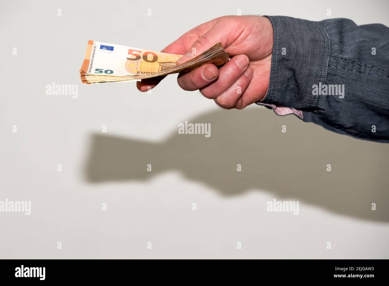 La mano maschile allungata dà un'ondata di banconote in euro. Operazioni di lavoro e di affari in attività economica non dichiarata di economia ombra Foto Stock