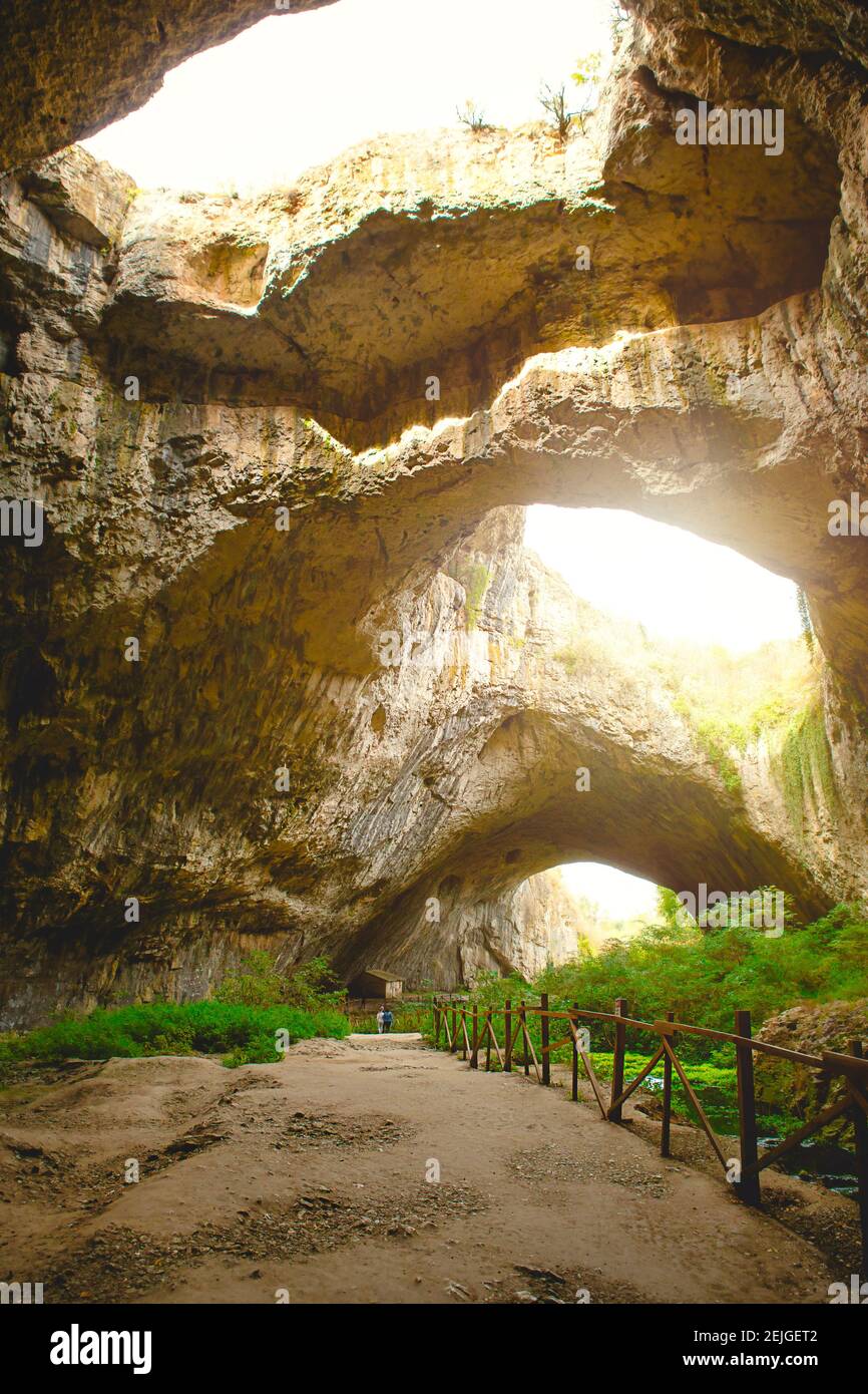 Devetashka grotta in Bulgaria - attrazione naturale. Alti archi di una  enorme grotta di pietra con fori rotondi in cima, una strada turistica con  una recinzione all'interno del Foto stock - Alamy