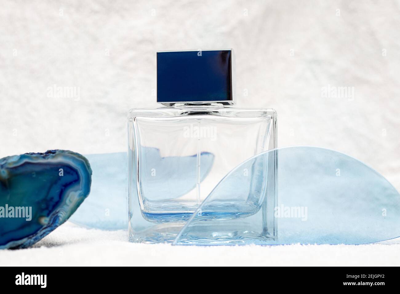 Bottiglia di vetro profumo o aftershave per gli uomini tra astratti blu derive su fondo bianco neve. Rinfrescante concetto di eau de toilette Foto Stock