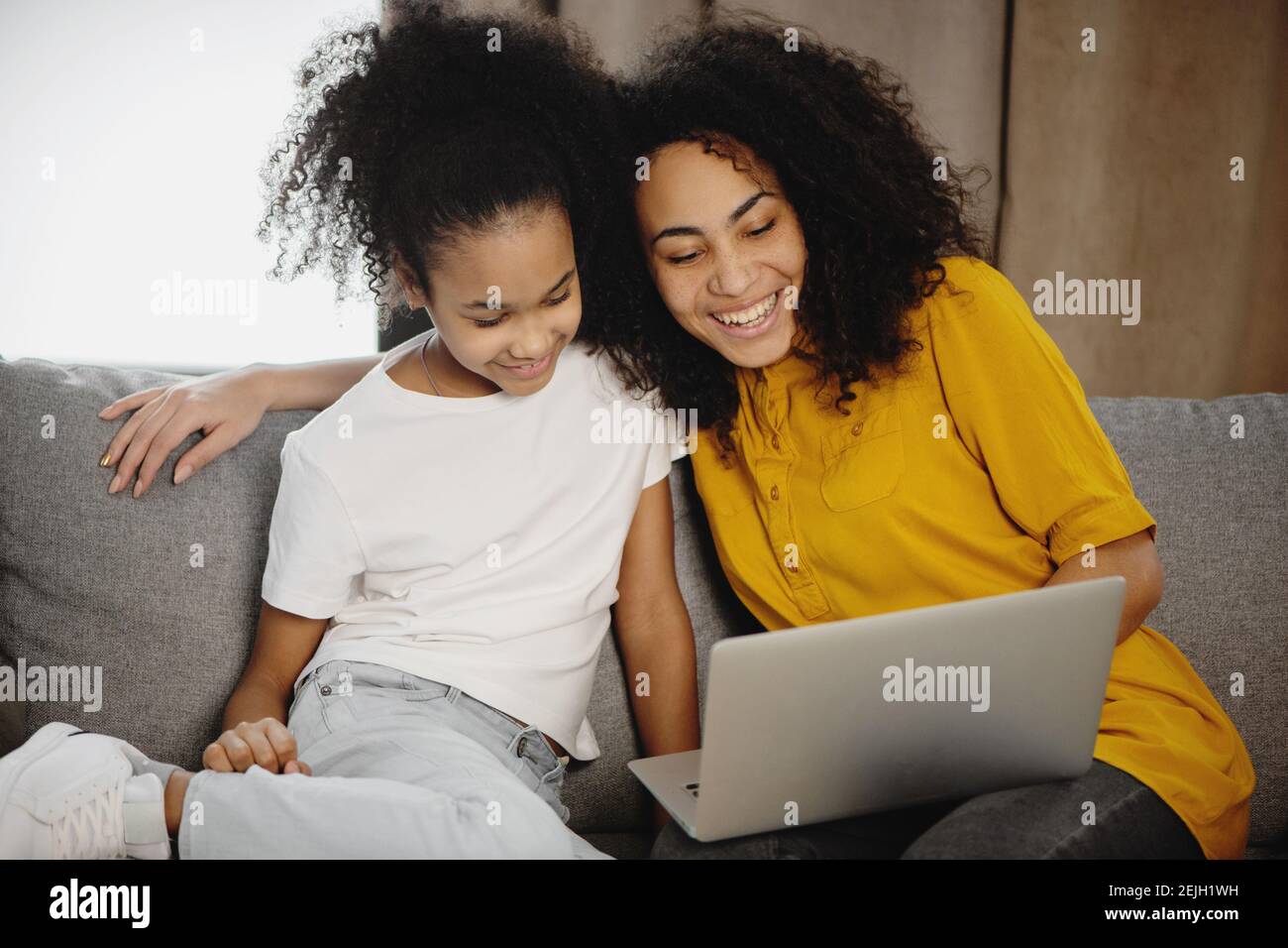 Madre afroamericana e figlia seduti sul divano a casa utilizzando un computer portatile. Foto Stock