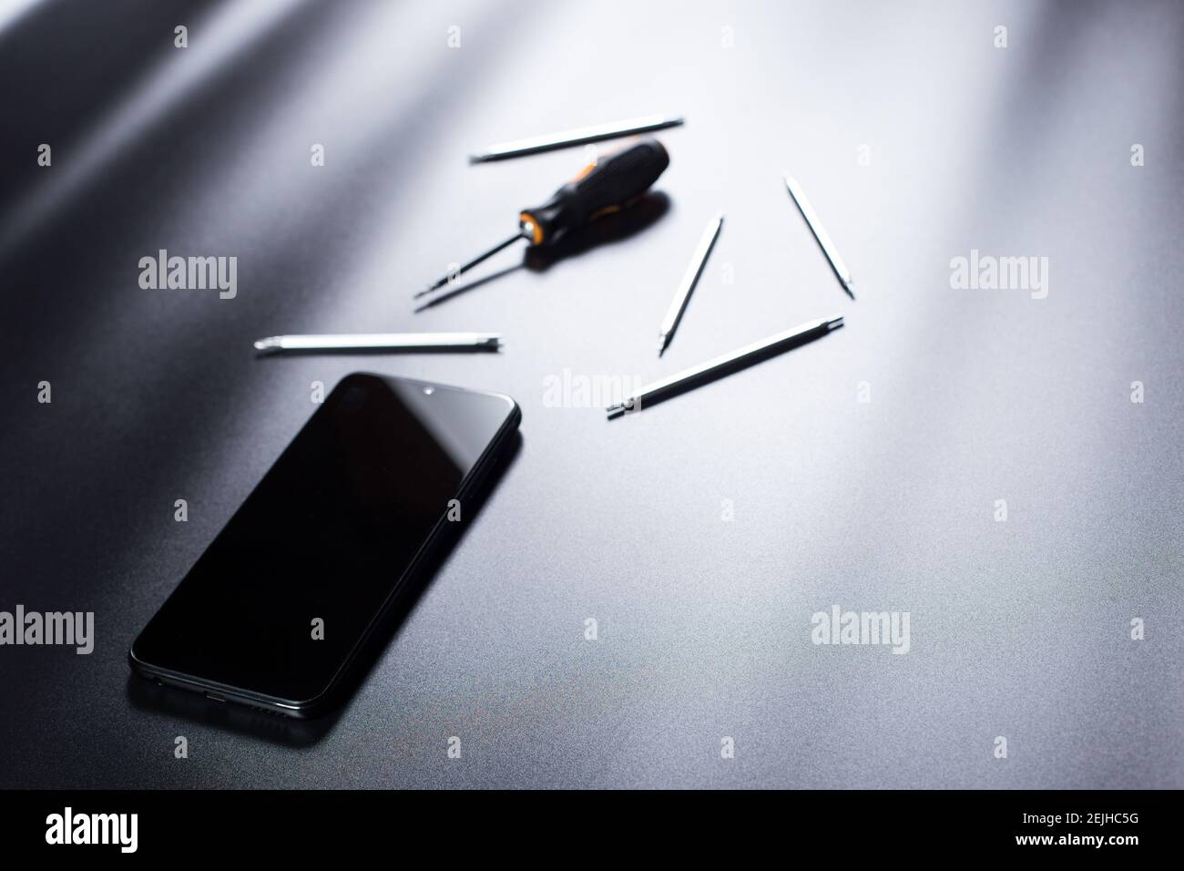 Smartphone nero con piccoli cacciaviti di riparazione elettronici su sfondo nero con spazio per la copia. Foto Stock