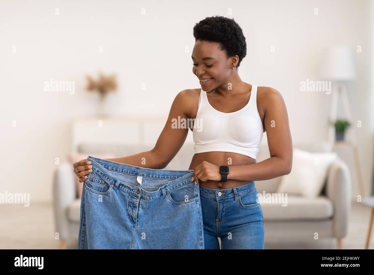 Black Lady che tiene i jeans troppo grandi dopo la perdita di peso a casa Foto Stock