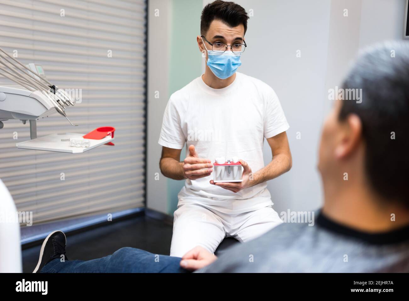 Chirurgo dentale con corona dentale in mani modello parla al paziente di protesi. Uomo su appuntamento del dentista Foto Stock