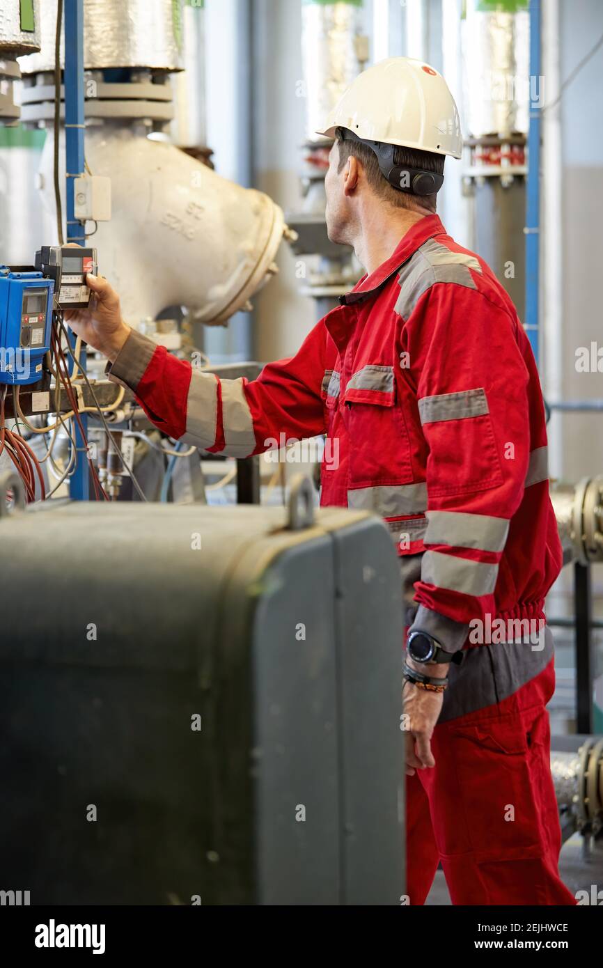 Tema del settore energetico: Un tecnico con tute rosse e casco bianco controlla i parametri di riscaldamento sui termometri. Manutenzione e ispezione. Foto Stock