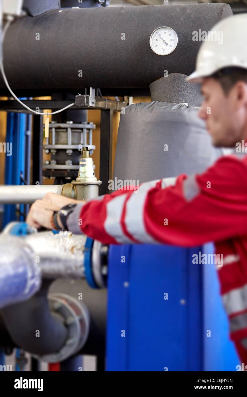 Tema del settore energetico: Un tecnico vestito di rosso e un casco bianco che controlla i parametri di riscaldamento. Tecnologia di distribuzione dell'acqua di riscaldamento. Foto Stock