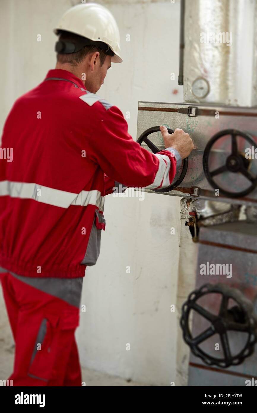 Tema del settore energetico: Un tecnico con tute rosse e casco bianco controlla i parametri di riscaldamento sui termometri. Manutenzione e ispezione. Foto Stock