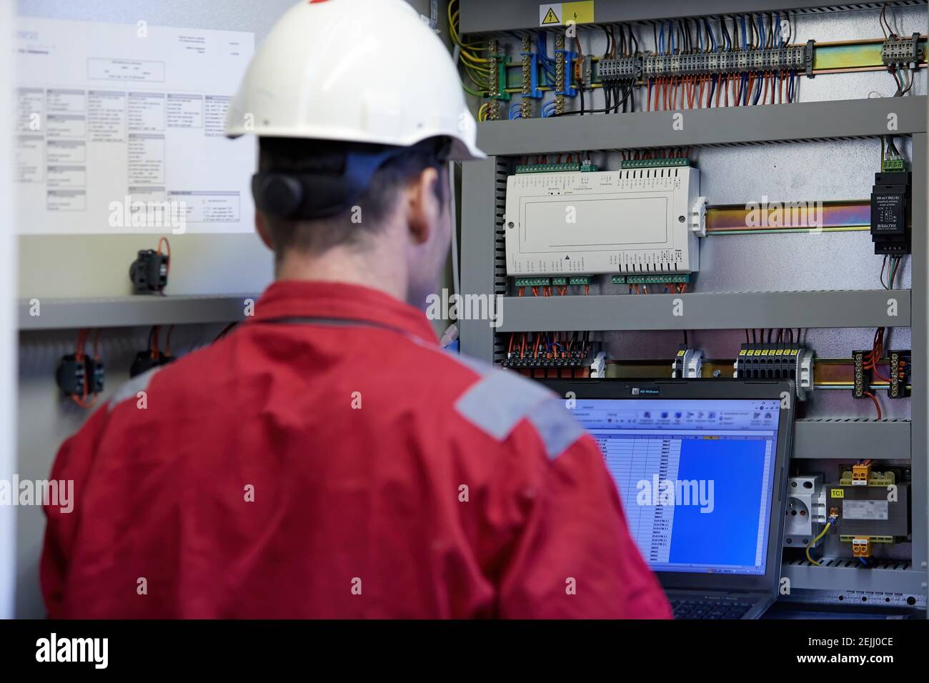 Tema del settore energetico: Un tecnico vestito con tute rosse e un casco bianco che controlla i parametri di riscaldamento su un computer portatile. Apparecchiature di riscaldamento Foto Stock