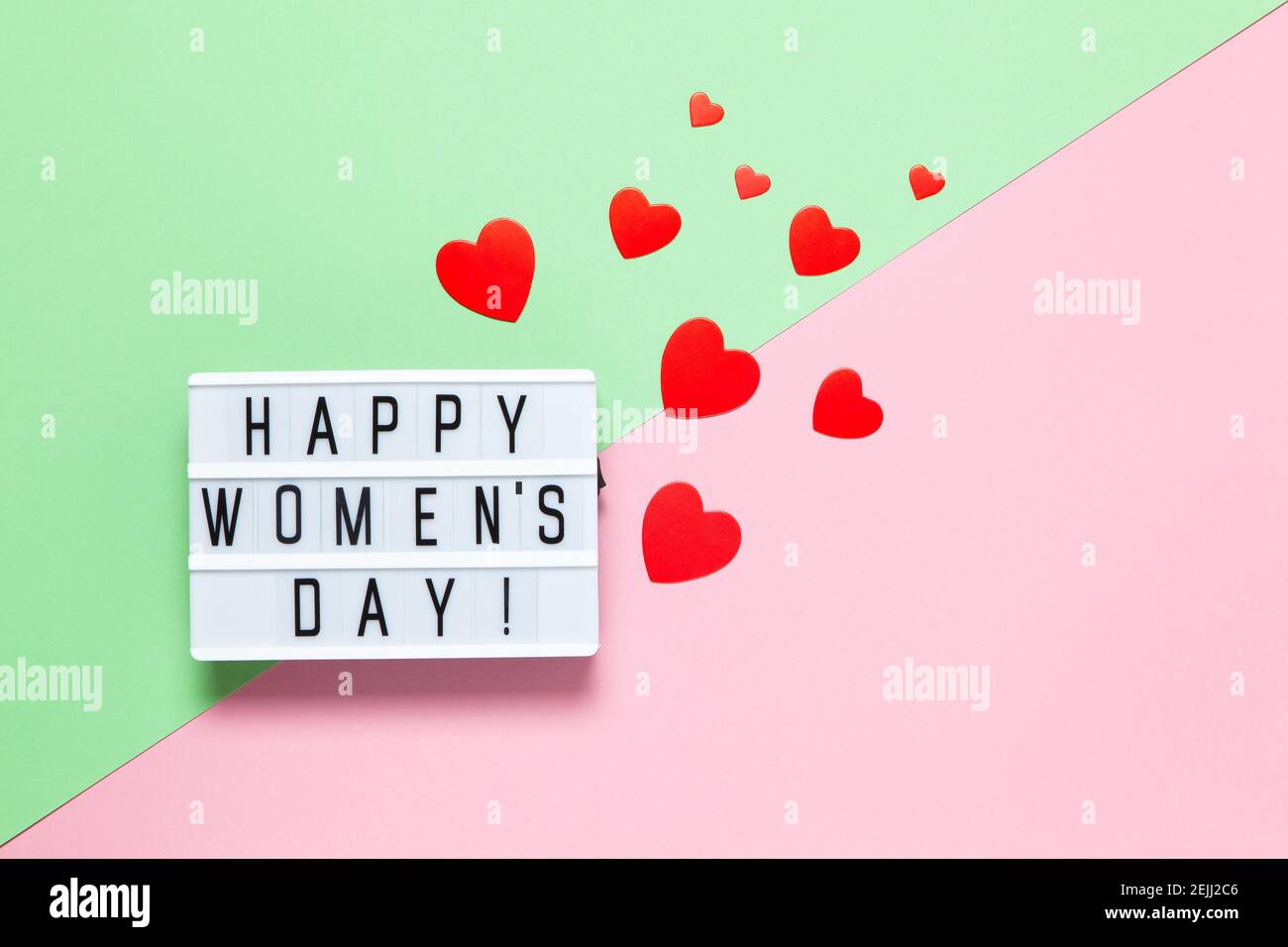 Lavagna luminosa con iscrizione Happy Women's Day, molto rosso cuori di diverse dimensioni su sfondo pastello rosa e verde, spazio copia. Orizzontale. Interno Foto Stock